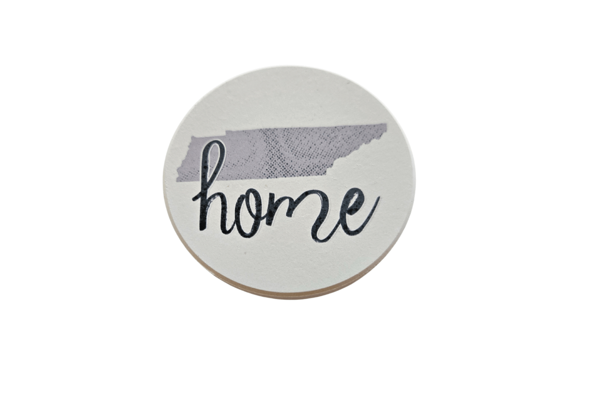 A ceramic coaster with 'Home' written in a cursive script, predominantly in gray and white colors.