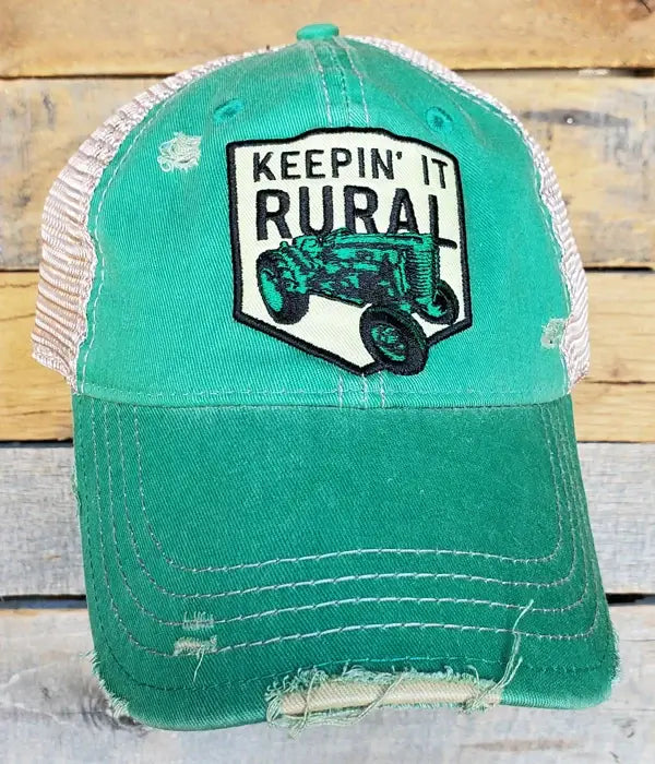 A green trucker hat with 'Keepin' It Rural' embroidered on the front and a distressed finish.