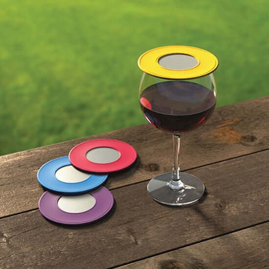 Colorful ventilated wine glass covers on a wine glass and table, featuring yellow, purple, blue, and pink designs.